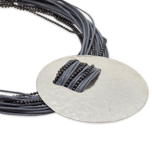 A silver hammered disc necklace pendant hosted by a grey cord. 